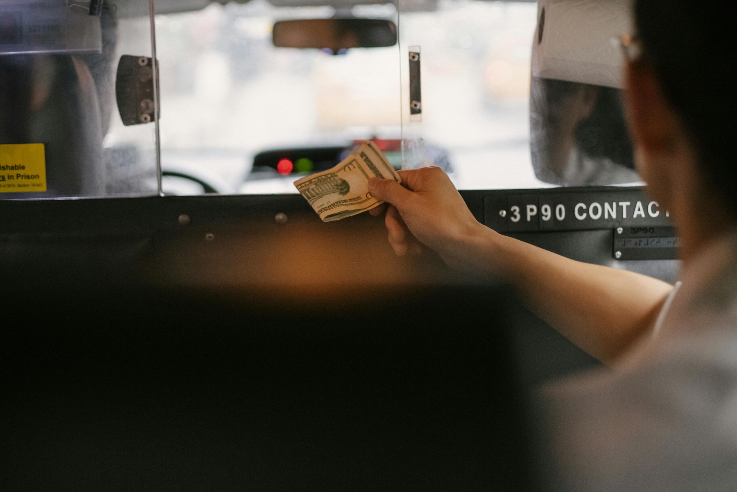 Closeup of a person handing cash to a taxi driver through the partition during a ride in a busy city.